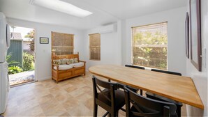 A dining area with a wooden table and chairs, a wooden bench with cushions, and a view through large windows. - Family Friendly 3BR Getaway! Central, Convenient, & Charming. (San Diego)