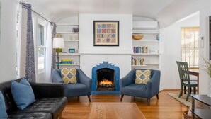 A living room with a fireplace, two armchairs, a sofa, a coffee table, and a bookshelf. - Family Friendly 3BR Getaway! Central, Convenient, & Charming. (San Diego)