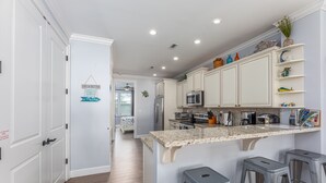Eine moderne Küche mit weißen Schränken, Granit Arbeitsplatten und Edelstahlgeräten. Drei Barhocker und eine kleine Kücheninsel mit Spüle sind vorhanden.