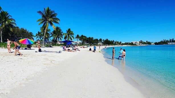 Ein Strand mit klarem türkisblauem Wasser, Palmen und Menschen, die sich sonnen.