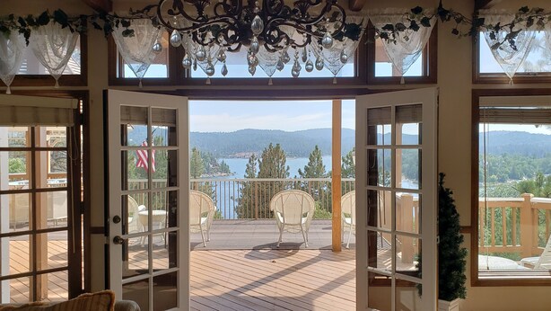 Ein offener Balkon mit Korbstühlen, einer Holzdielenveranda und Blick auf einen See und Berge.