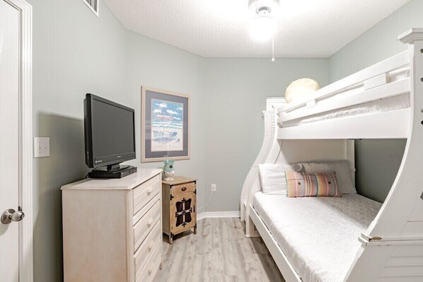 A bedroom with a bunk bed, a television on a dresser, and a framed picture on the wall.