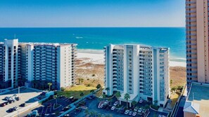 Et højt hotel med flere etager, parkeringsplads og udsigt til stranden.