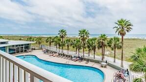 A pool area with lounge chairs and palm trees, overlooking a beach.