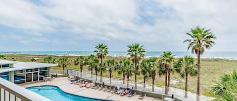 A pool area with lounge chairs and palm trees, overlooking a beach.