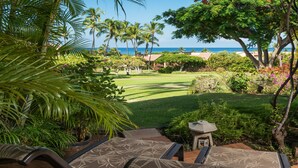 A tropical garden with a view of the ocean, featuring lounge chairs and a stone lantern.