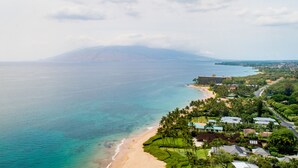 An aerial view of a coastal area with a beach, residential buildings, and a mountain in the background.
