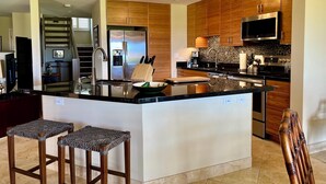 A modern kitchen with a central island, stainless steel appliances, wooden cabinets, and a chandelier.