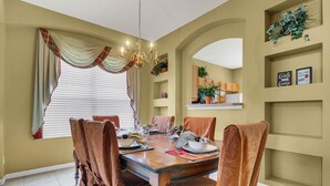 A dining area with a wooden table, brown upholstered chairs, a chandelier, and a window with blinds. - Work & Play Here-Gated Resort Villa-5 Masters-Private Pool-Free Wifi-Near Disney (Davenport)