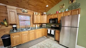 A kitchen with wooden cabinets, a stainless steel refrigerator, a microwave, an oven, and a coffee maker. - Log Cabin On 5 Private Acres, Gated Community With River Access (Rutherfordton)