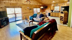 A spacious living area with a wooden ceiling, a sofa, a coffee table, and a television. - Log Cabin On 5 Private Acres, Gated Community With River Access (Rutherfordton)