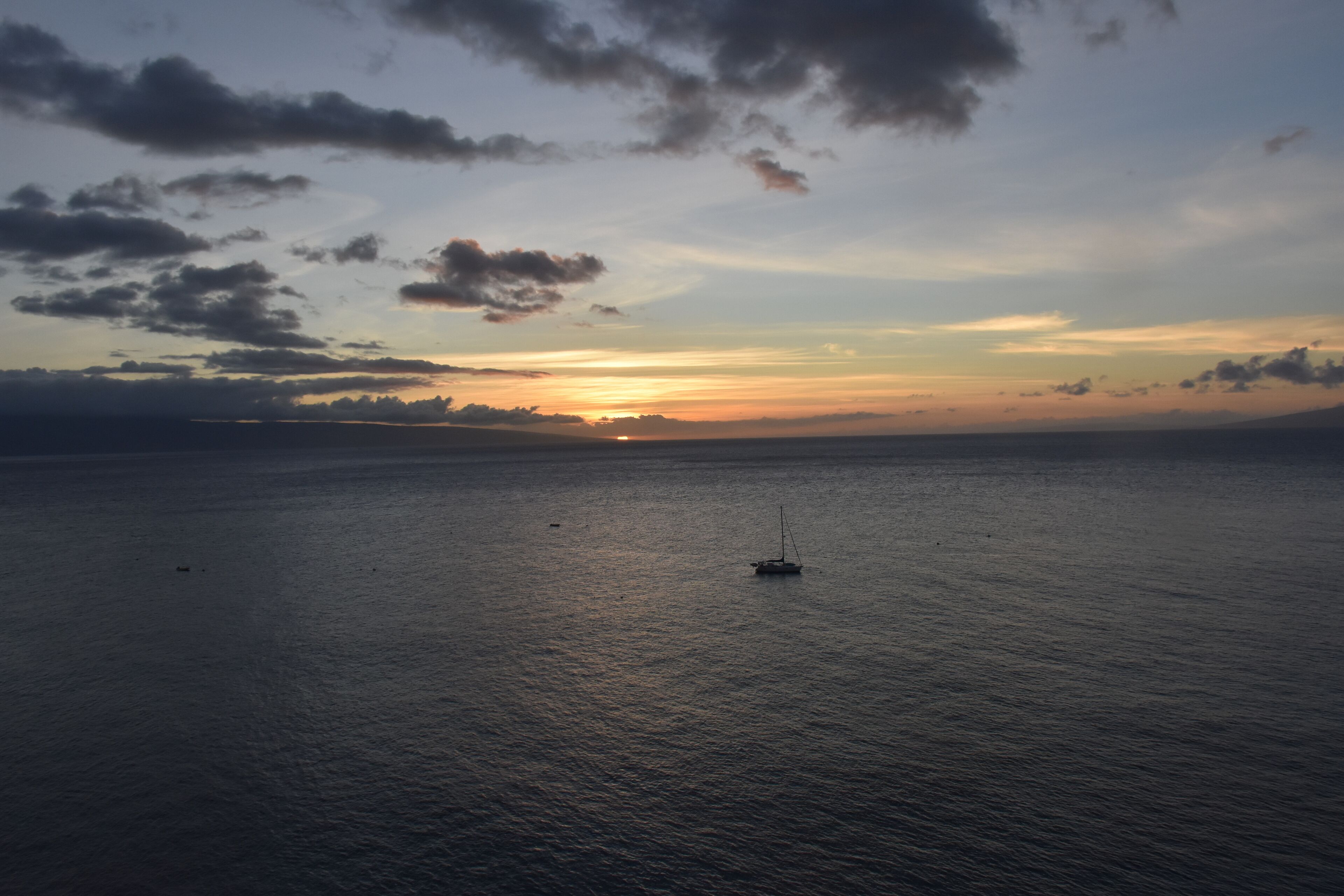 Une mer calme au coucher du soleil, avec un voilier à l’horizon.