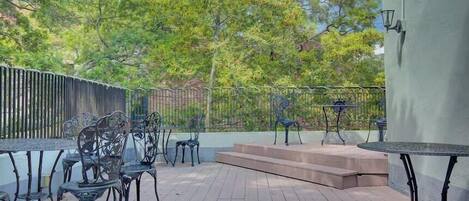 Un patio al aire libre con sillas y mesas de metal, una terraza de madera y una barandilla de metal.