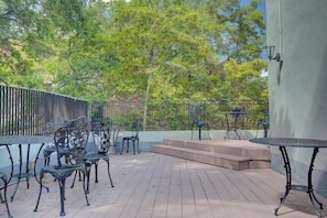 Une terrasse extérieure avec des chaises et des tables en métal, une plateforme en bois et une rambarde en métal.