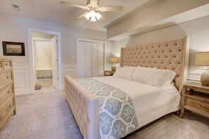 Une chambre à coucher avec un grand lit, une commode, un ventilateur de plafond et une porte donnant sur une salle de bain.