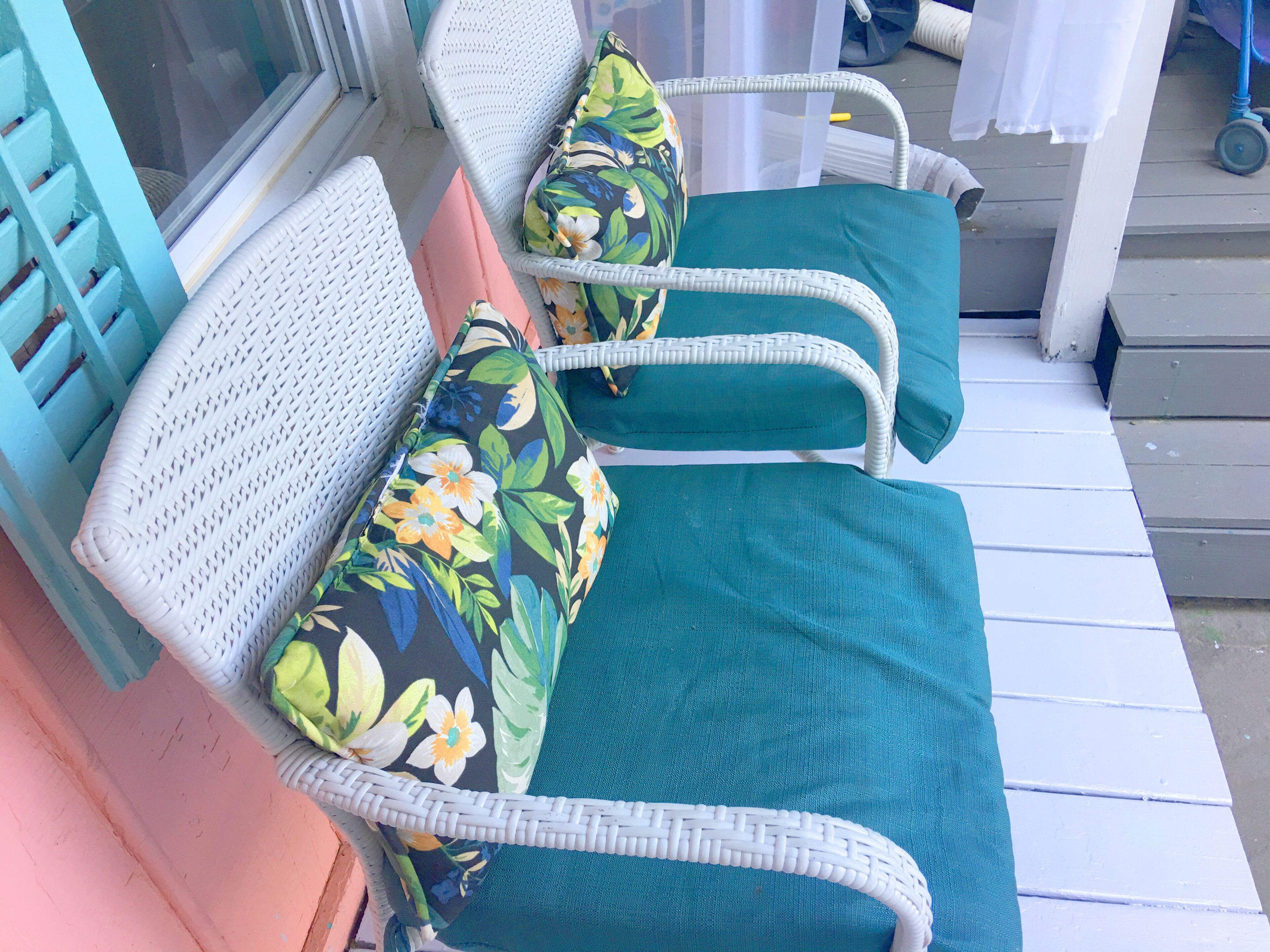 A row of white wicker chairs with teal cushions and floral patterns, arranged on a wooden deck.