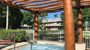 Uma área de piscina com um pérgola de madeira, uma escada de piscina de metal e uma cerca branca.
