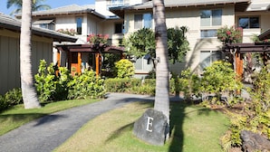 Um edifício residencial de vários andares com um jardim bem cuidado, incluindo palmeiras e diversos arbustos.