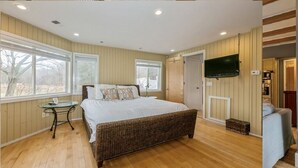 A bedroom with a large bed, wooden flooring, a television mounted on the wall, and a window providing a view of the outdoors. - Warren Dunes - Large 2 Br-2 Bath, Hot Tub, Wbfpl , Next To Wineries (Bridgman)