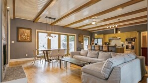 A spacious living room with a large gray sofa, wooden flooring, and a kitchen area in the background. - Warren Dunes - Large 2 Br-2 Bath, Hot Tub, Wbfpl , Next To Wineries (Bridgman)