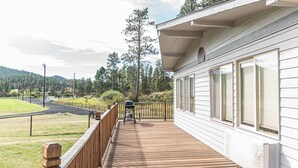 Ett trädäck med en grill, ett inhägnat område och utsikt över en väg och en skog.