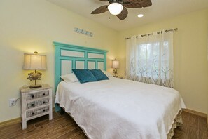 A bedroom with a bed, a nightstand, a ceiling fan, and a window with curtains.