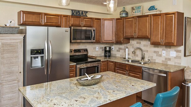 A modern kitchen with wooden cabinets, stainless steel appliances, a granite countertop, and blue bar stools.