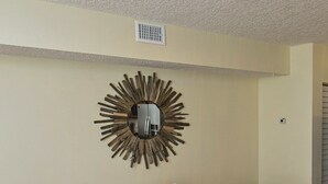 A dining area with a table and four chairs, a ceiling vent, and a wall-mounted decorative mirror.
