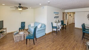 A spacious living room with a blue sofa, matching chairs, a wooden coffee table, and a ceiling fan.