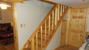 A wooden staircase leading to a loft bedroom with a wooden door and a bed with a blue and white patterned bedspread.