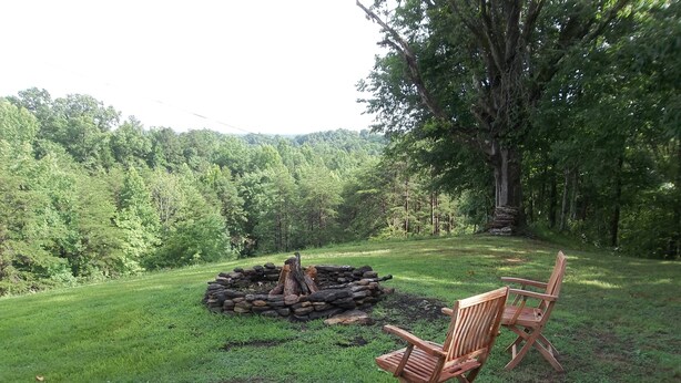 A grassy outdoor area with a stone fire pit and two wooden chairs.