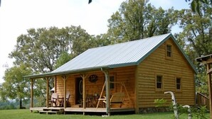 A log cabin with a porch, outdoor seating, and a metal roof.