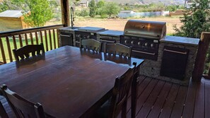 An outdoor patio with a wooden table and chairs, a built-in grill, and a stone fireplace. - Luxury Log Home Retreat near Zion National Park (Toquerville)