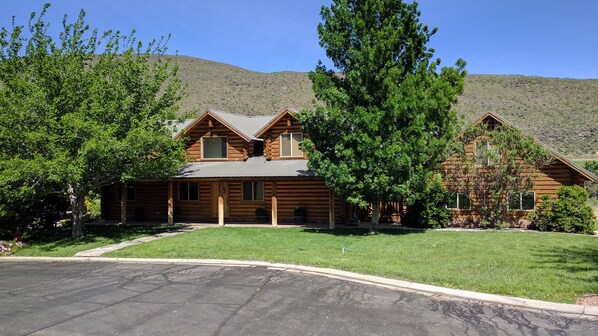 A log cabin with a front porch, a garage, and a well-maintained lawn. - Luxury Log Home Retreat near Zion National Park (Toquerville)