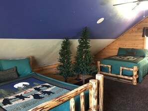 A cozy room with a sloped ceiling, two beds with matching green bedding, a small artificial tree, and a rug with animal silhouettes. - Luxury Log Home Retreat near Zion National Park (Toquerville)