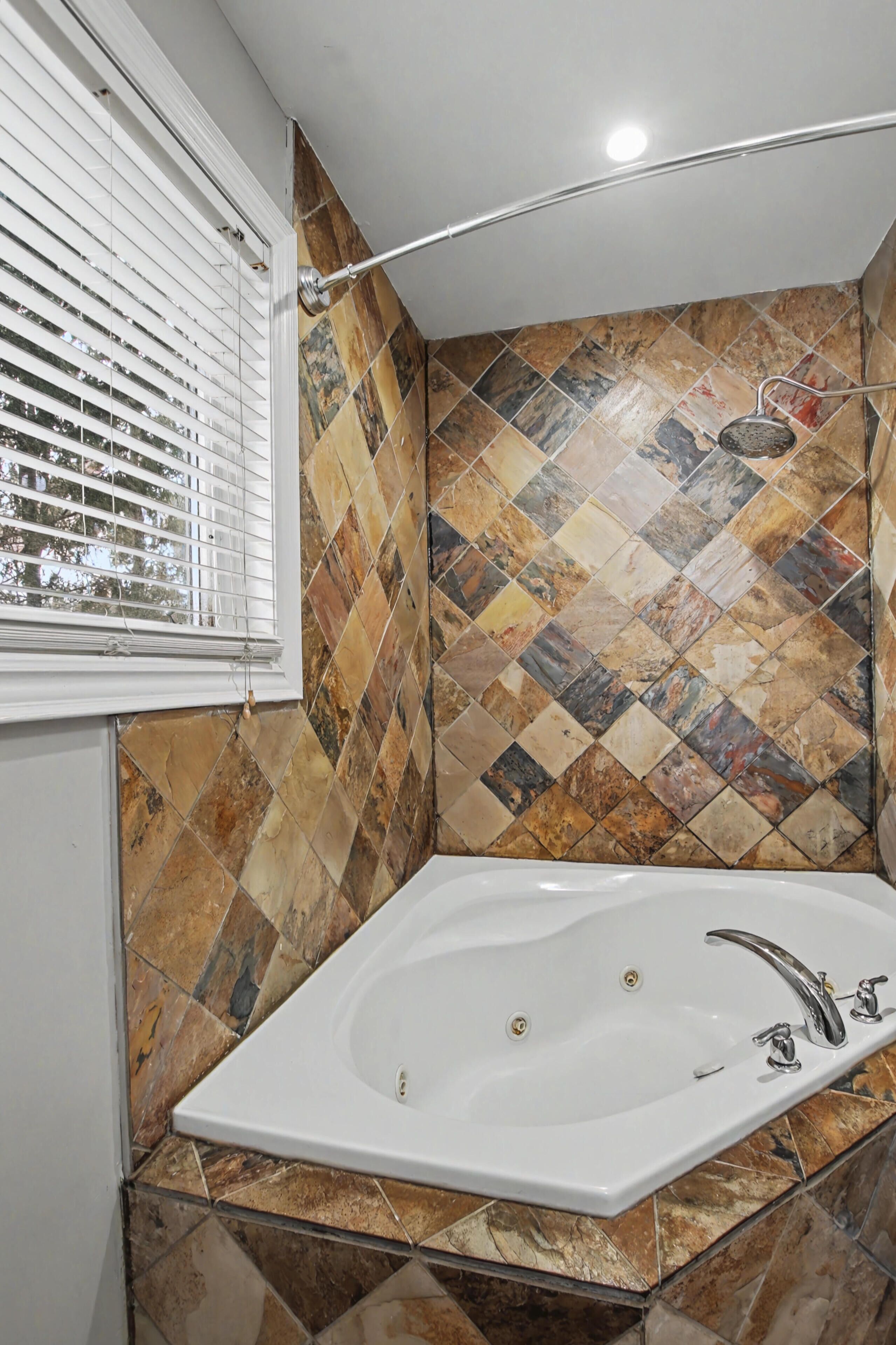 Une salle de bain avec une baignoire sur pieds, une fenêtre avec des stores et un mur carrelé orné d’un motif géométrique.