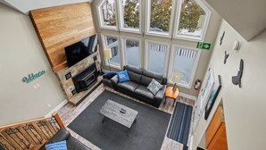 A spacious living area with a fireplace, a sofa with cushions, a coffee table, and large windows offering a view of the outdoors. - Executive Blue Mountain Chalet, 6 Bedrooms, Sauna (Blue Mountains)