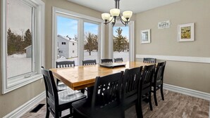 A dining area with a wooden table and black chairs, large windows, and a chandelier. - Executive Blue Mountain Chalet, 6 Bedrooms, Sauna (Blue Mountains)