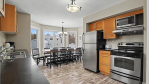 A modern kitchen with stainless steel appliances, wooden cabinets, and a dining area with a table and chairs. - Executive Blue Mountain Chalet, 6 Bedrooms, Sauna (Blue Mountains)