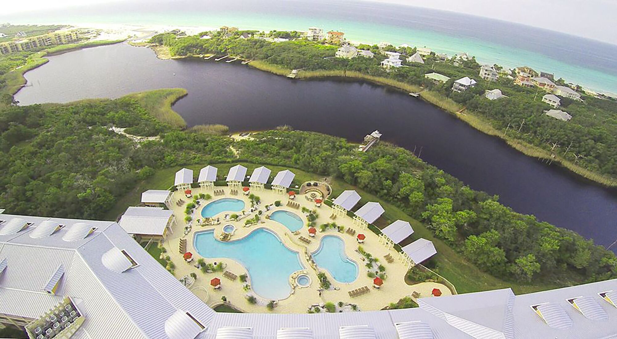 Vista aérea de um resort com várias piscinas, um porto para iates e vegetação exuberante.