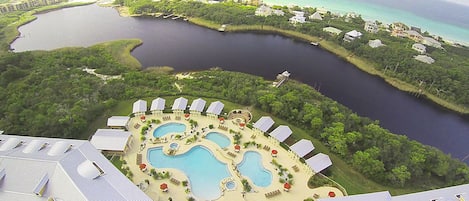 An aerial view of a resort with multiple swimming pools, a marina, and lush greenery.