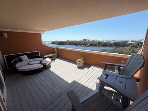 A balcony with a wooden floor, a sofa, a chair, and a potted plant. - Waterfront Ocean View 2 Story 3BR Top Floor Luxury Condo - Sanctuary at Redfish  (Santa Rosa Beach)
