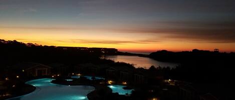 Un resort con varias piscinas, una masa de agua y edificios al fondo.