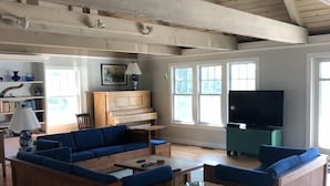 Un ampli saló amb sostre de fusta, un sofà modular gran, un arçòs blanc i una televisió.