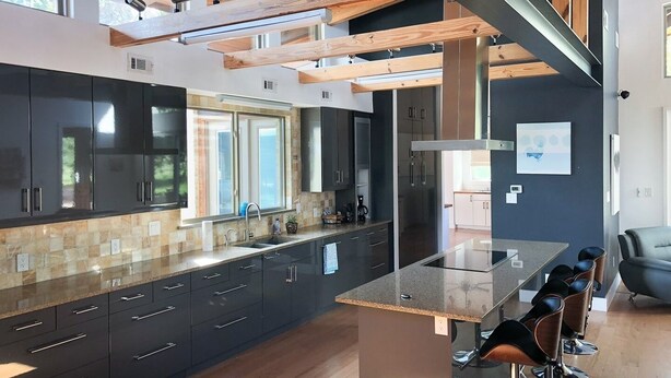 A modern kitchen with dark cabinets, a large island, and a dining area with bar stools. - Modern Austin Retreat Getaway - exquisite home! (Round Rock)