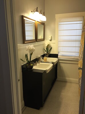 Un bagno con un mobile lavabo nero, due lavabi, uno specchio e una finestra con persiane.