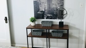 Habitación con arte mural de paisaje urbano, una consola de madera con cestas, una planta en maceta y ropa de cama estampada.