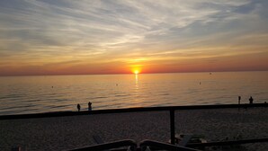 Ein Strand mit Sonnenuntergang über dem Ozean, einer Geländer und ein paar Personen in der Ferne.