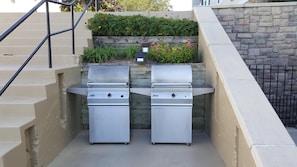 Outdoor cooking area with two barbecue grills and a staircase leading to a garden.