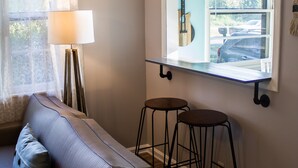 En hyggelig stue med en sofa, to barstole, en lampe og et vindue med et 'GATHER' skilt.